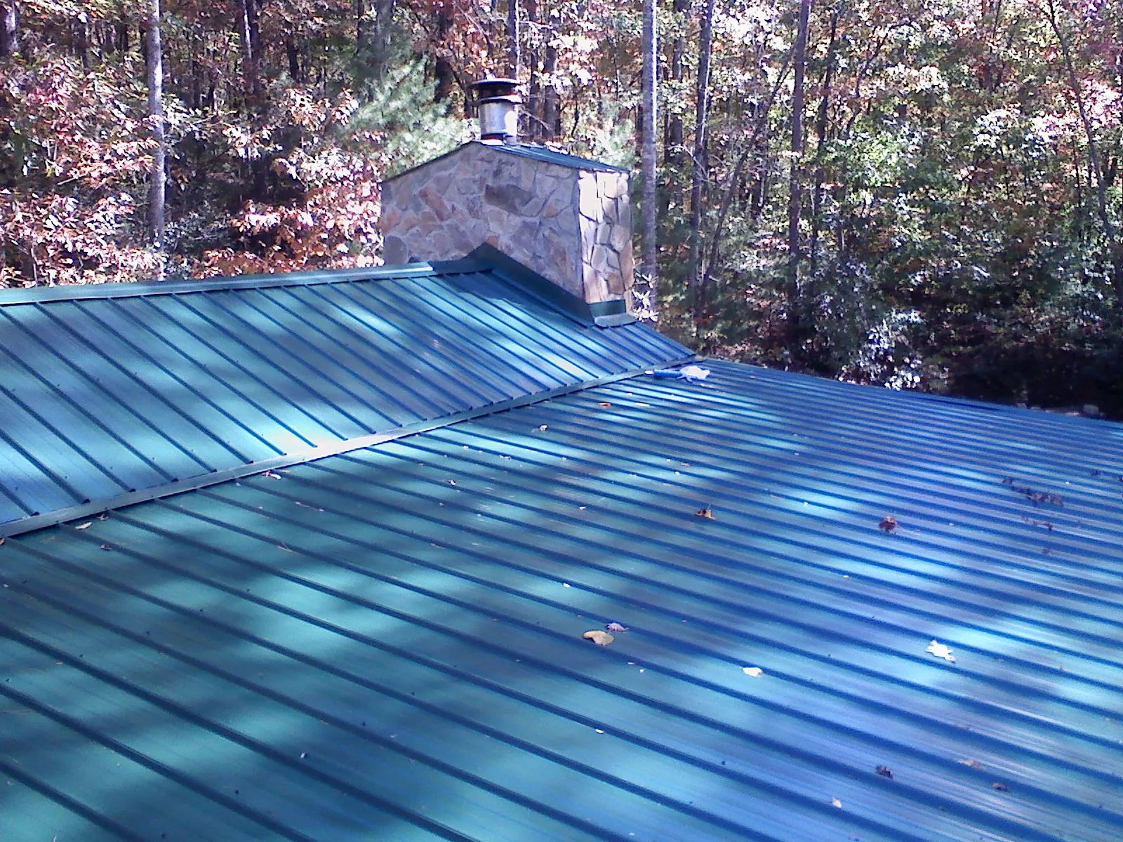New green metal roof and stone chimney surrounded by autumn woods in Rome